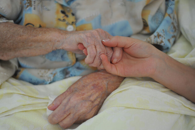 Erweiterung des Palliativ-Pflegeteams – ein junger Mensch hält die Hand eines alten Menschen
